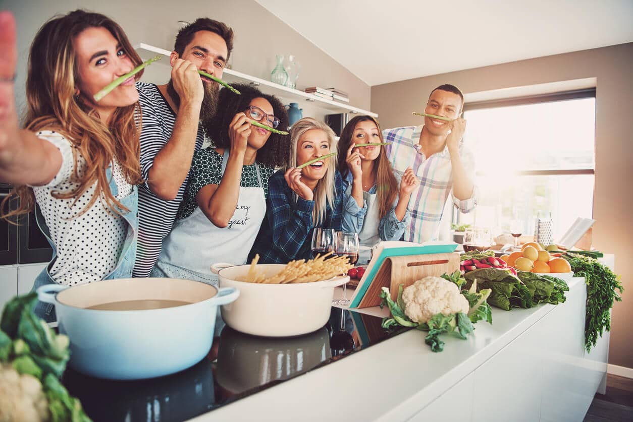 6 Freunde stehen in Küche und tragen Spargelstangen unter die Nase